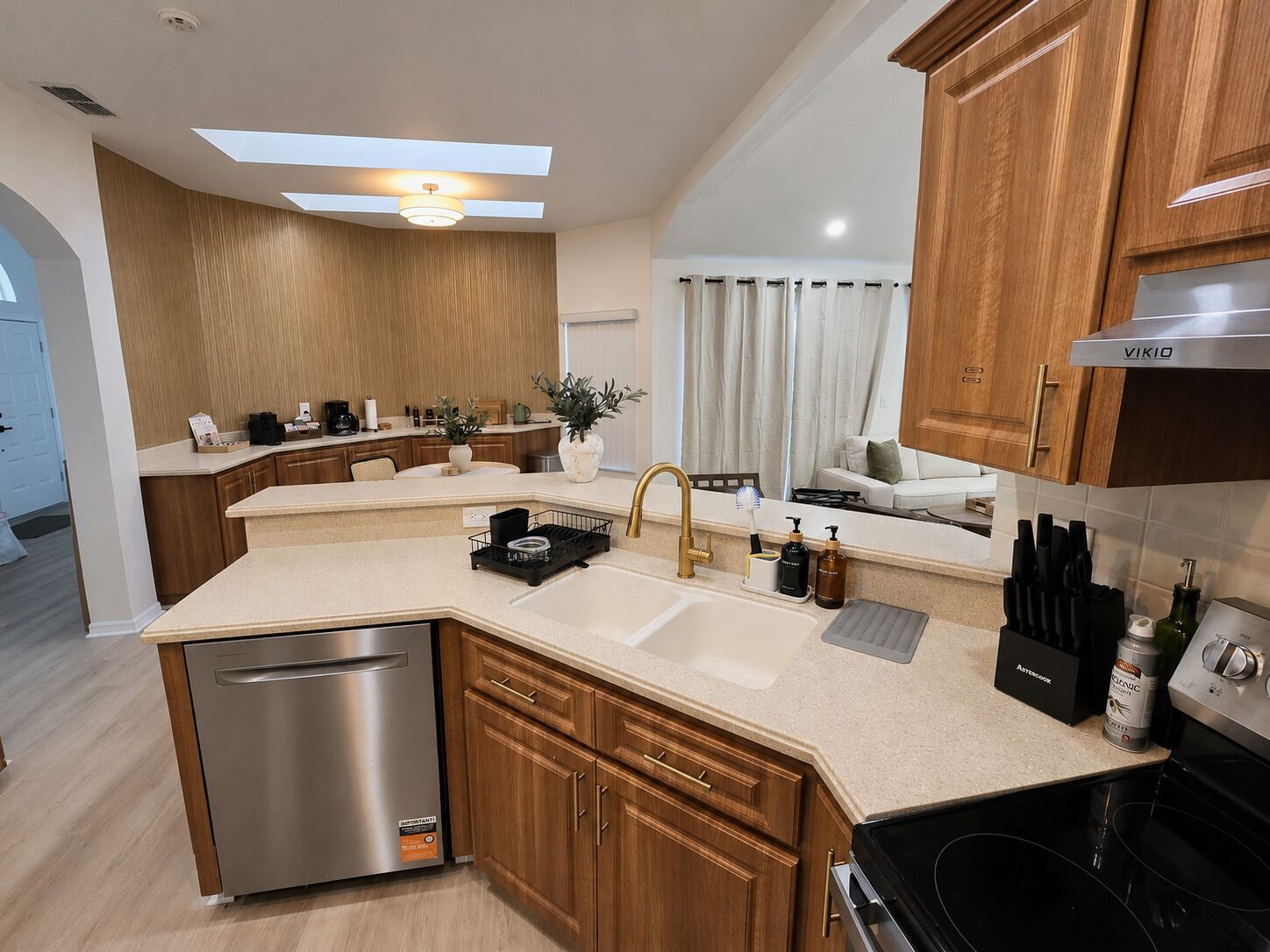 A modern kitchen with a dishwasher, sink, and stove. There is a dining area with a white table and chairs.