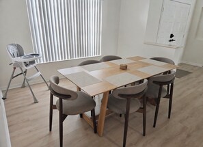 A dining area with a rectangular table, six chairs, and a high window with vertical blinds. - Sand and Sage: 3BR, 2BH, Heated Pool, Fenced Yard (Spring Hill)