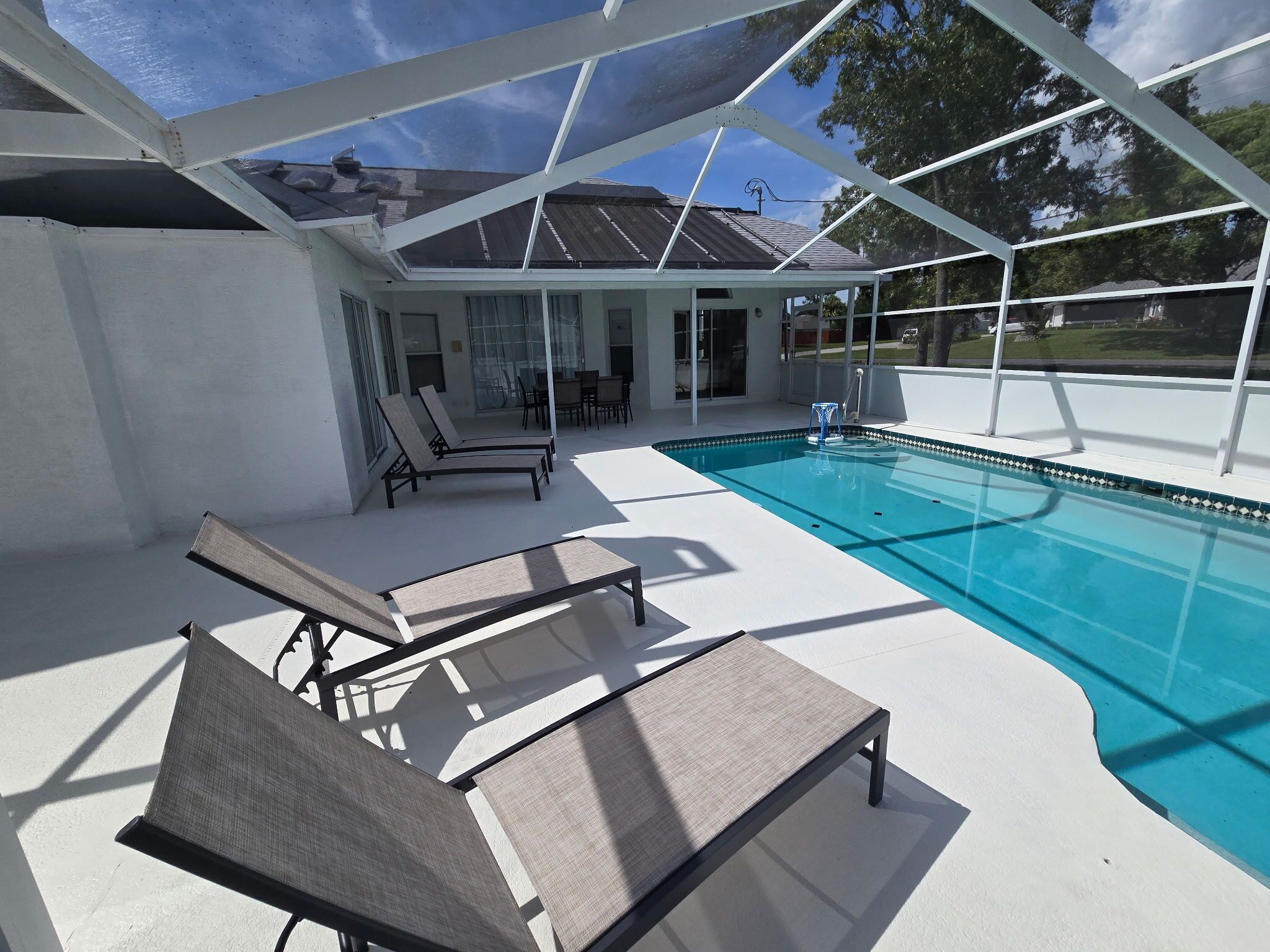 A covered outdoor swimming pool area with lounge chairs and a patio.