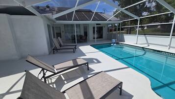 A covered outdoor swimming pool area with lounge chairs and a patio.