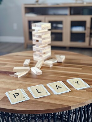 Ein Holztisch mit gestapelten und umgestürzten Jenga-Steinen sowie Spielkarten, die das Wort 'PLAY' bilden.