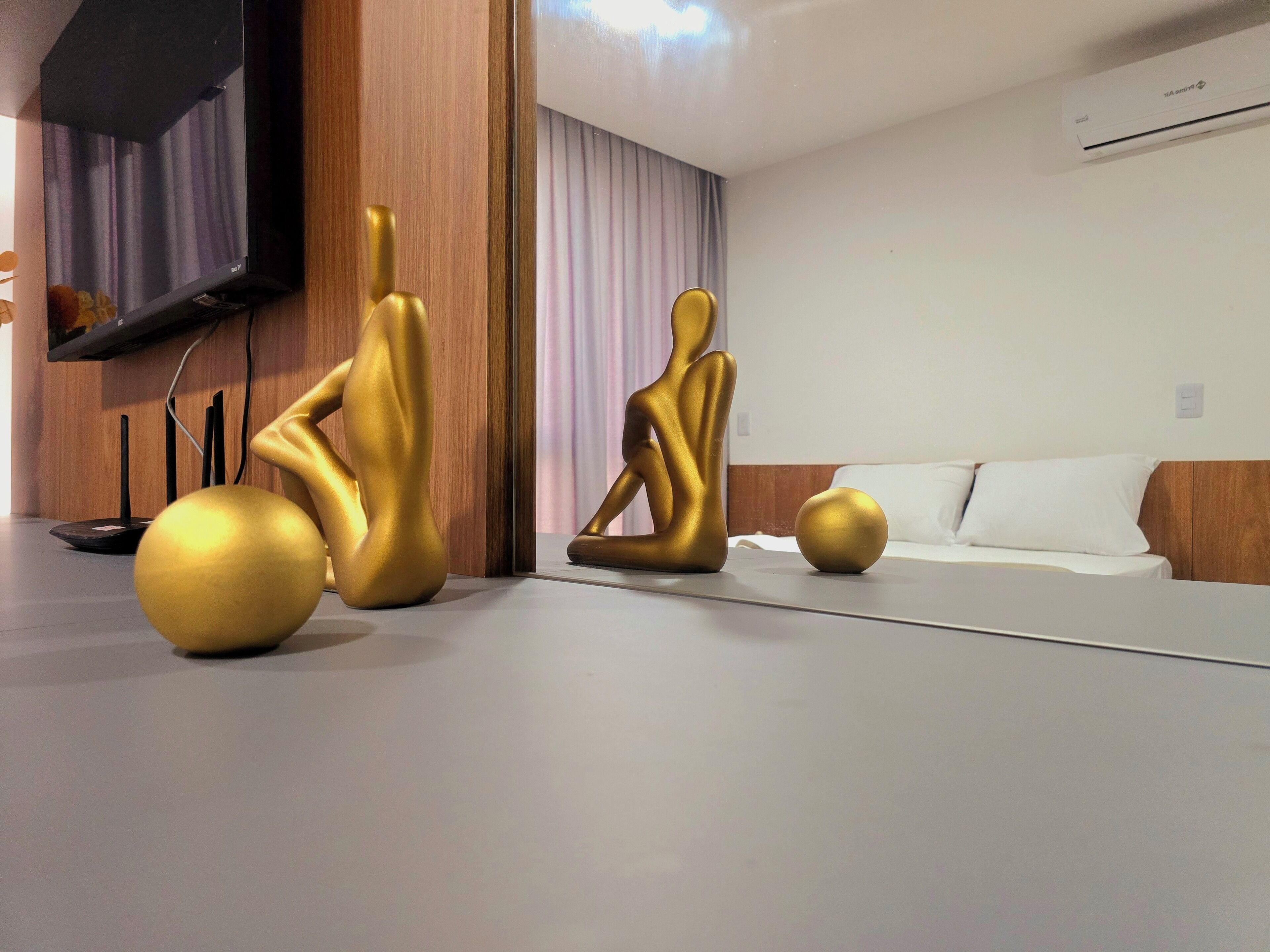 Een moderne kamer met een flatscreen televisie aan de muur, een bank en twee gouden beelden op de vloer.