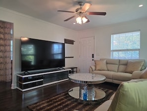A living room with a flat-screen TV, a ceiling fan, a sofa, and a round coffee table. - Pet Friendly, Short Drive to Beach, Nearby Stores! (Galveston)