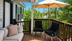 A covered porch with a wooden deck, a beige sofa with cushions, two black armchairs, and a large beige umbrella providing shade. - Pet Friendly, Short Drive to Beach, Nearby Stores! (Galveston)