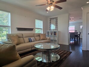 Ein Wohnzimmer mit einer Couch, einem runden Glastisch, einem Deckenventilator und einem Bücherregal.