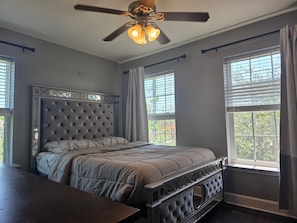 A bedroom with a tufted headboard, a bed with patterned bedding, a wooden nightstand, and a ceiling fan with lights. - Pet Friendly, Short Drive to Beach, Nearby Stores! (Galveston)