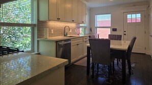 A modern kitchen with white cabinets, a built-in dishwasher, and a dining area with a table and chairs. - Pet Friendly, Short Drive to Beach, Nearby Stores! (Galveston)