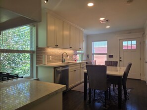A modern kitchen with white cabinets, a built-in dishwasher, and a dining area with a table and chairs. - Pet Friendly, Short Drive to Beach, Nearby Stores! (Galveston)