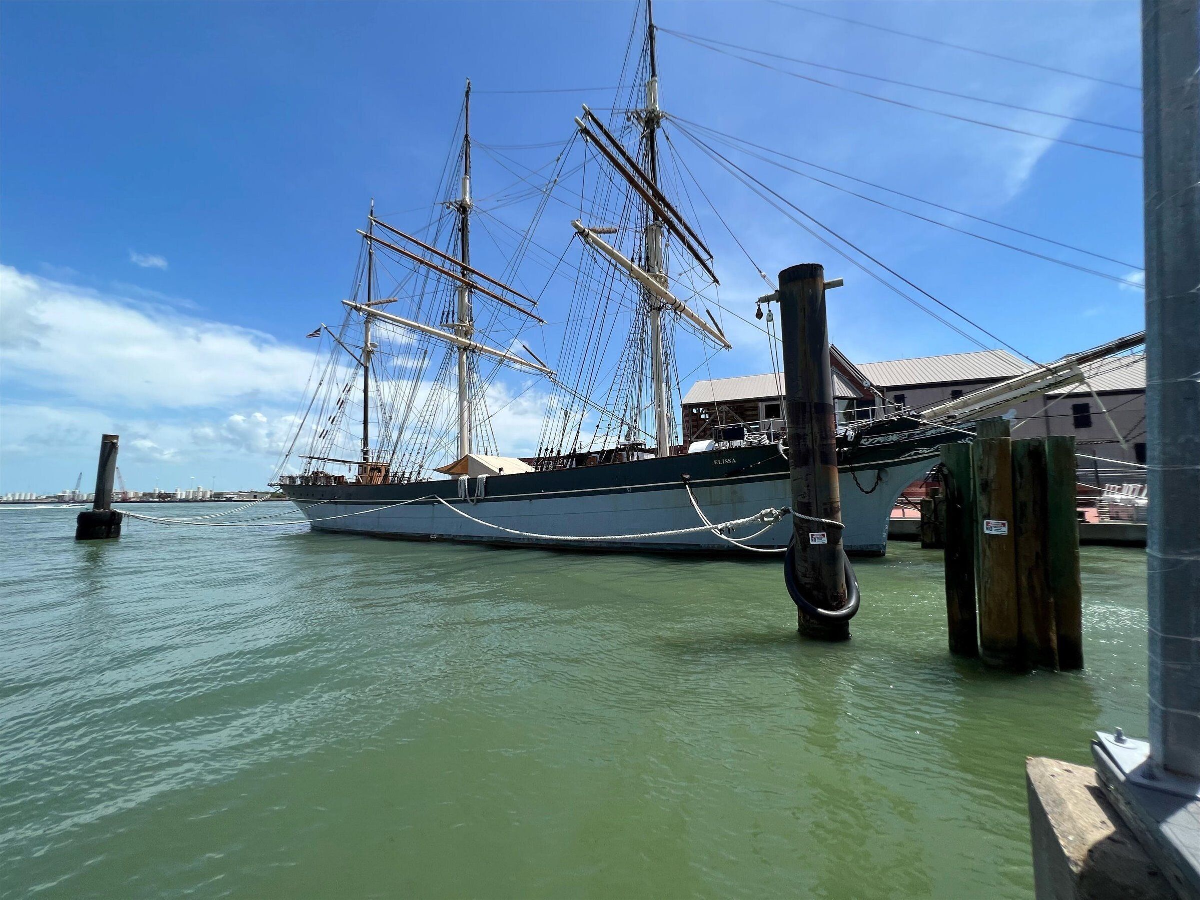 Ein großes Segelschiff liegt in einer Marina vor Anker, der Himmel ist wolkenlos und das Wasser ruhig.