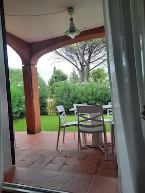 An outdoor patio area with a table and chairs, a ceiling fan, and a view of a garden with trees and shrubs. - Cozy vacation home 250 meters from the beach, with reserved parking and free Wi-Fi (Cannigione)