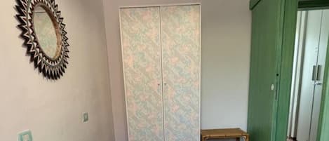 A room with two beds, a mirror, a wardrobe, and a bench.