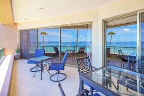A balcony with a glass table and chairs, overlooking a pool and the ocean. - Sonoran Spa E302 Beachfront 2BR Condo (Puerto Peñasco)