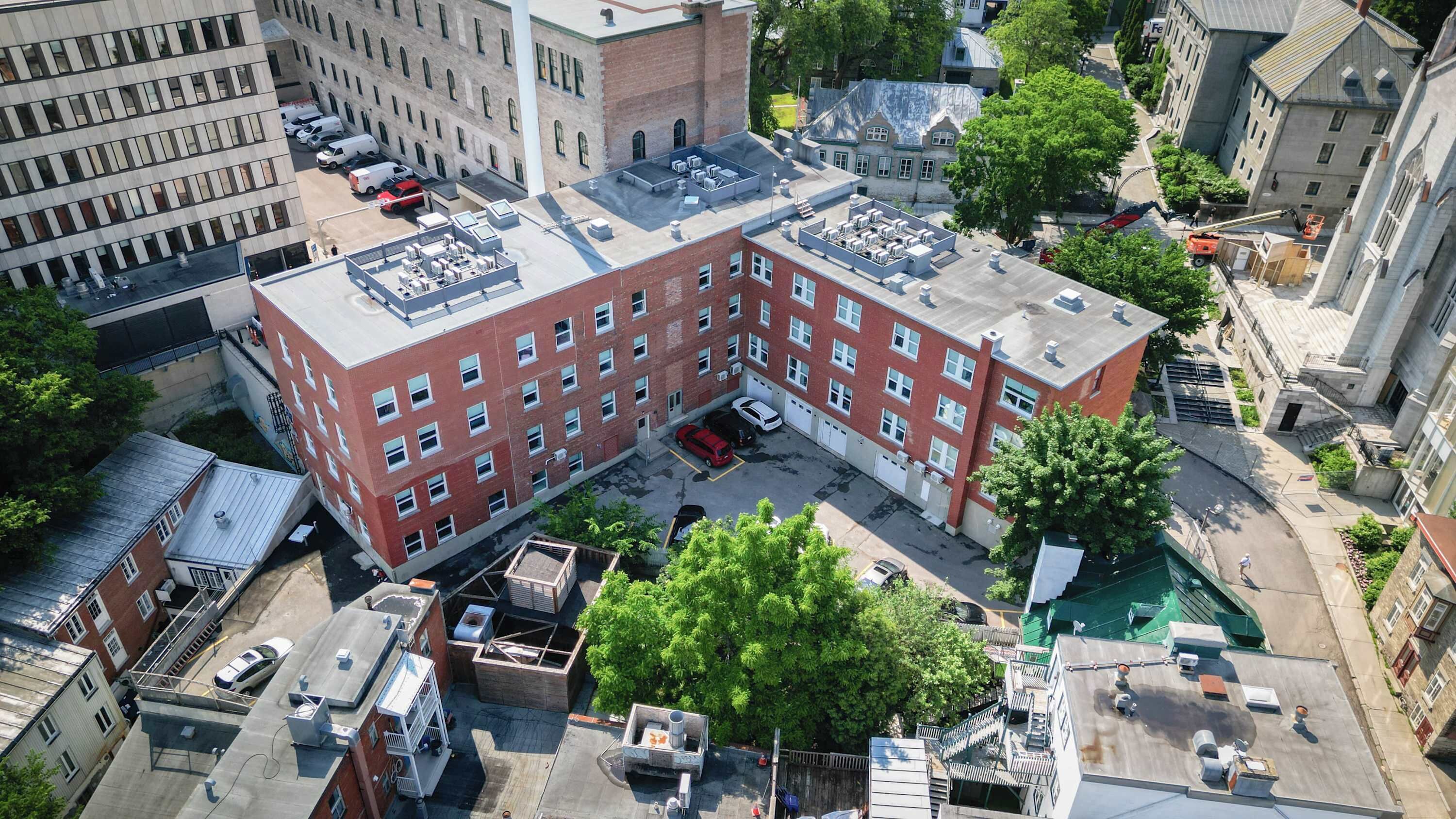 A multi-story building with a rooftop terrace, parking area, and surrounding trees.