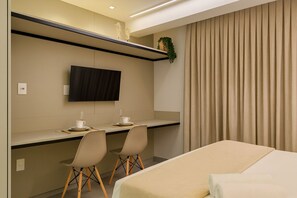 Habitación de hotel con cama, escritorio con dos sillas, televisor de pantalla plana y ventana con cortinas.