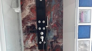 En dusch med en svart kontrollpanel och en vägg av marmor.