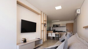 Una sala moderna con un televisor de pantalla plana, un comedor con sillas y una cocina con microondas.