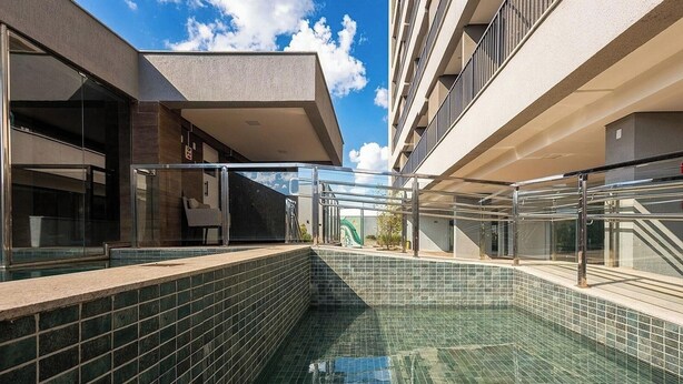 Una piscina moderna al aire libre con una barandilla de cristal, rodeada de edificios con balcones.