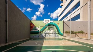 Una cancha de baloncesto al aire libre con un mural, rodeada de edificios.