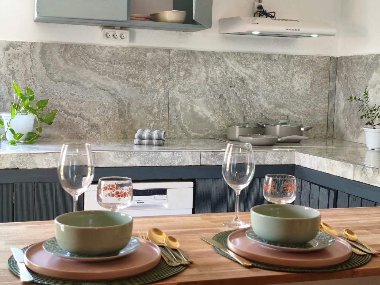 Une cuisine moderne avec un revêtement mural en marbre, une table à manger dressée avec des assiettes, des bols et des verres à vin.
