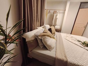 A neatly made bed with pillows and a blanket, a bedside table with a lamp, and a plant in the corner. - Pliana Secret Garden: Cozy 2-bedroom house in serene Le Gosier with AC (Le Gosier)