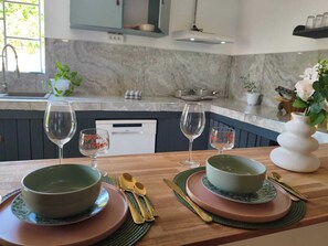 A modern kitchen with a marble backsplash, a dishwasher, and a dining area with a wooden table set for two. - Pliana Secret Garden: Cozy 2-bedroom house in serene Le Gosier with AC (Le Gosier)