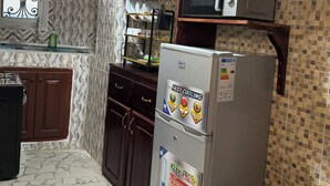 A kitchen with wooden cabinets, a microwave, a refrigerator, and a patterned backsplash. - Premium 2 Bedroom Apt | Plus Parking & Views (Yaoundé)