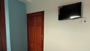 A bedroom with a bed, a wooden door, a wall-mounted TV, and a light switch. - Premium 2 Bedroom Apt | Plus Parking & Views (Yaoundé)