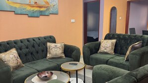 A living room with a green sofa set, two round tables, and a wall clock. - Premium 2 Bedroom Apt | Plus Parking & Views (Yaoundé)