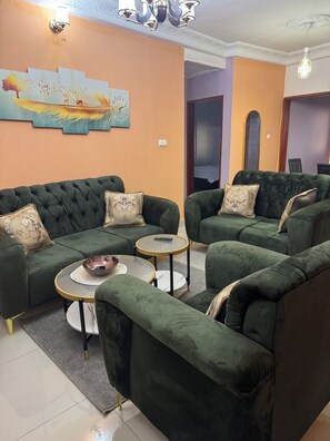 A living room with a green sofa set, two round tables, and a wall clock.
