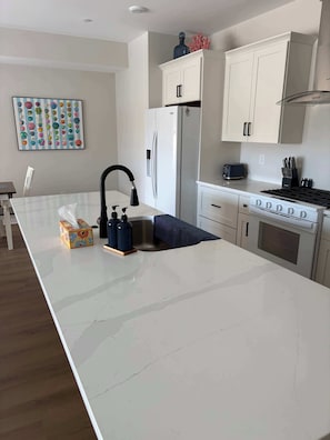 Et moderne køkken med marmor bordplade, rustfrie stål apparater og hvide skabe.