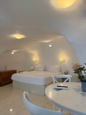 Ein Schlafzimmer mit zwei Betten, einem Nachttisch, einem Sessel, einem Tisch und einer Zimmerpflanze.