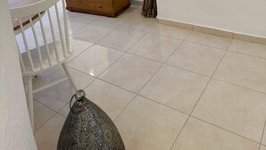 Ein Zimmer mit einem weißen Sofa, einer Holzkiste, einer Vase mit Zweigen und einem weißen Sessel.
