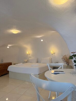 Ein Zimmer mit gewölbter Decke, zwei Betten mit weißen Bettwäsche, einem kleinen runden Tisch mit einer Fernbedienung und einem weißen Stuhl.