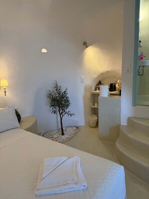 Ein Hotelzimmer mit einem Bett, einer kleinen Topfpflanze, einem Badezimmer mit Waschbecken und Spiegel sowie einer Treppe.