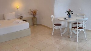 Ein Hotelzimmer mit einem Bett, einem runden Esstisch mit Stühlen, einer Vase mit Trockenpflanzen und Wandleuchten.