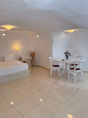 Ein Hotelzimmer mit einem Bett, einem runden Esstisch mit Stühlen, einer Vase mit Trockenpflanzen und Wandleuchten.