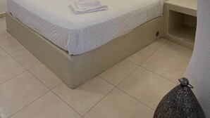 A neatly made bed with white linens and towels, a bedside table with a lamp, and a nightstand with a small decorative item. - Santo Caves Santorini Suite With Private Hot Tub (Santorini)