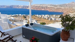 A balcony with a hot tub, seating, and a view of the sea and cliffs. - Santo Caves Santorini Suite With Private Hot Tub (Santorini)