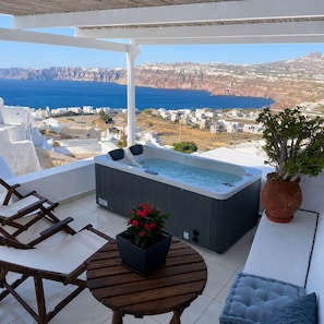 A balcony with a hot tub, seating, and a view of the sea and cliffs. - Santo Caves Santorini Suite With Private Hot Tub (Santorini)