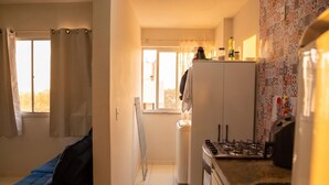 Cocina compacta con estufa a gas, refrigerador y ventana con cortinas.