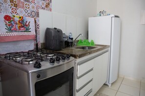 Una cocina con estufa a gas, refrigerador y pileta con escurreplatos verde.