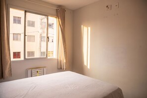 Quarto com uma cama de solteiro, janela com cortinas e radiador.