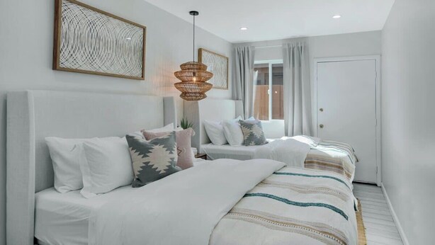 Een moderne slaapkamer met twee bedden, een hanglamp en een groot raam met gordijnen.