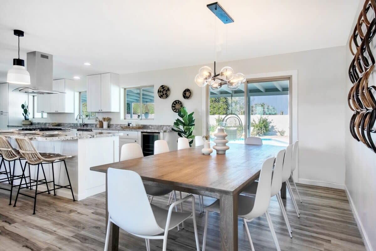 A modern kitchen with white cabinetry, a wooden dining table, and a view of a swimming pool.