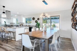 A modern kitchen with white cabinetry, a wooden dining table, and a view of a swimming pool. - 7BR Scottsdale Retreat | Pool, Casita & Lawn Games (Scottsdale)