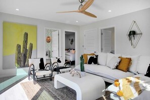 A modern living room with a white sofa, a coffee table, and a ceiling fan. - 7BR Scottsdale Retreat | Pool, Casita & Lawn Games (Scottsdale)
