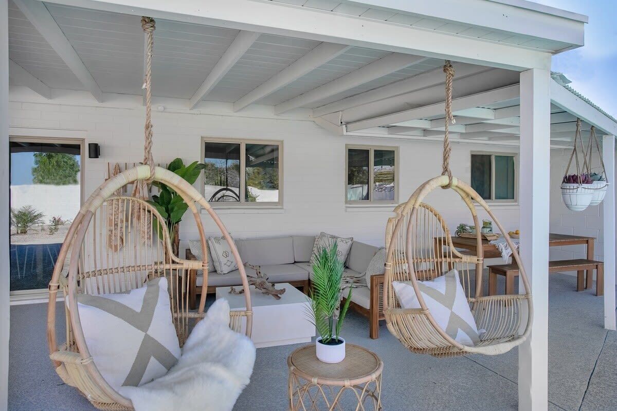 A covered outdoor seating area with wicker chairs and a sofa, a small round table, and a hanging basket.