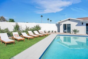 A swimming pool with lounge chairs and a building with a glass door. - 7BR Scottsdale Retreat | Pool, Casita & Lawn Games (Scottsdale)
