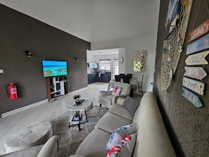 A living room with a sofa, a coffee table, and a television. There is a kitchen in the background. - Le Coin Grenadier (Flic en Flac)