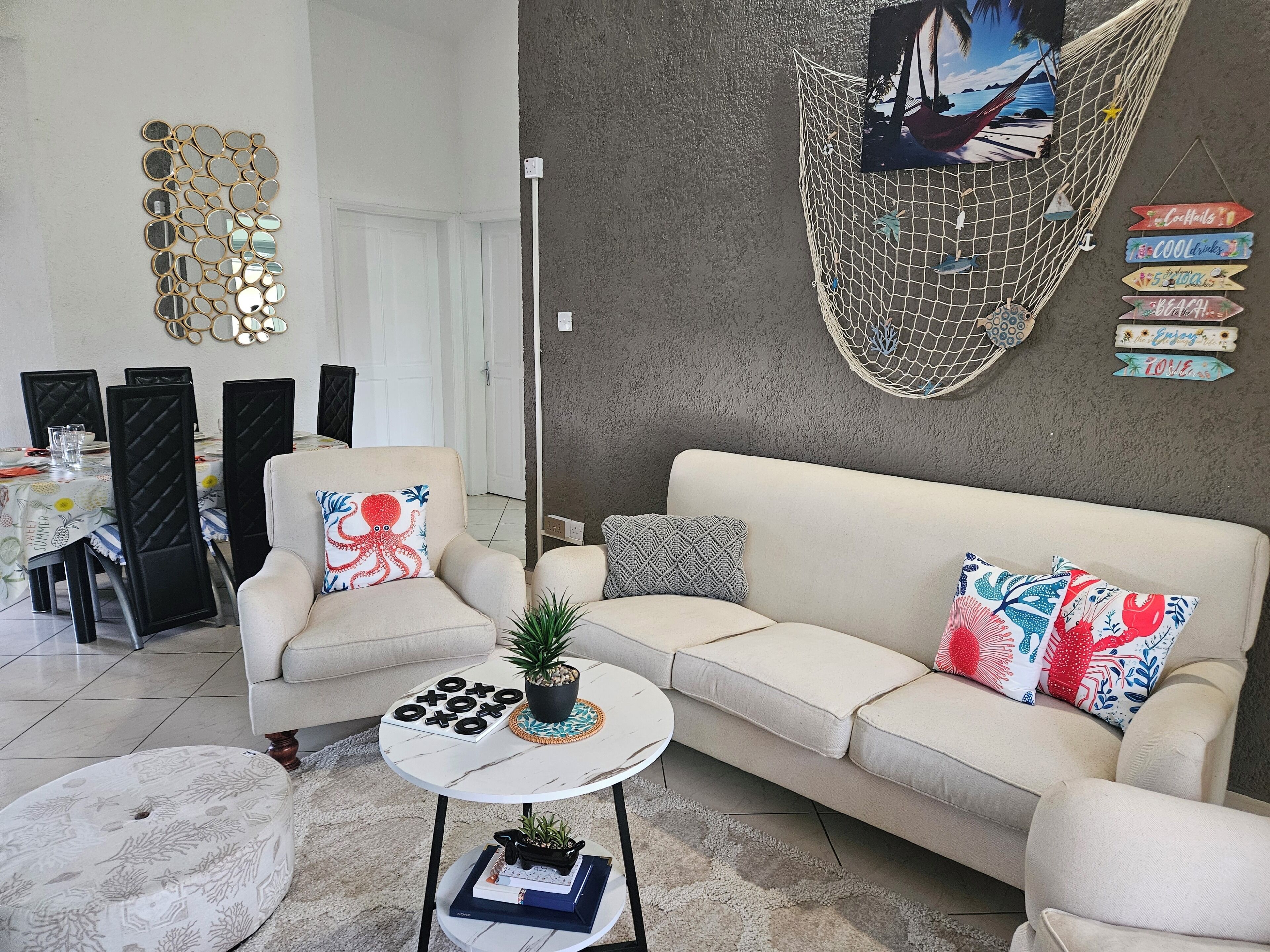 A living room with a sofa, coffee table, and chairs. There is a hammock, wall art, and a small table with a plant.